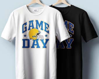 Könnte beinhalten: Zwei kurzärmelige T-Shirts, eines weiß und eines schwarz, hängen an Holzbügeln. Das weiße Shirt zeigt die Worte "GAME DAY" in Blau und Gelb mit einer Footballhelm-Grafik. Das schwarze Shirt hat das gleiche Design.