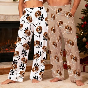 May include: White and tan pajama pants with a repeating pattern of a dog's face, paw prints, and hearts. The dog's name, "Bambi", is printed on the pants. The second pair of pants are tan with the same pattern.
