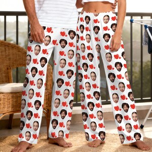 May include: White pajama pants featuring a repeating pattern of faces and red hearts. The pajama pants are a comfortable, casual style, suitable for lounging or sleeping. The faces and hearts are printed across the entire surface of the pants.
