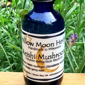 May include: A blue glass bottle with a dropper top, labelled "Willow Moon Herbs" and "Reishi Mushroom Double Extraction Tincture". The bottle is sitting on a wooden surface with green plants in the background.