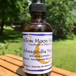 May include: A brown glass bottle with a dropper top and a white label that reads "Willow Moon Herbs Handmade in Wisconsin Ashwagandha Tincture Withania somnifera Ingredients: Ashwagandha Root, grain Willow Moon ~ Green Bay, WI willowmoonherbs.com"