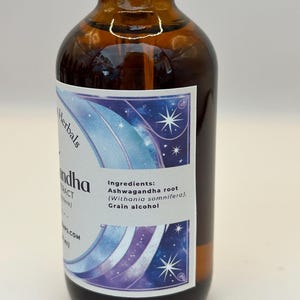 May include: A brown glass bottle with a label that says "Herbals Ashwagandha Extract (Withania somnifera). Grain alcohol" and has a purple and blue design with stars.