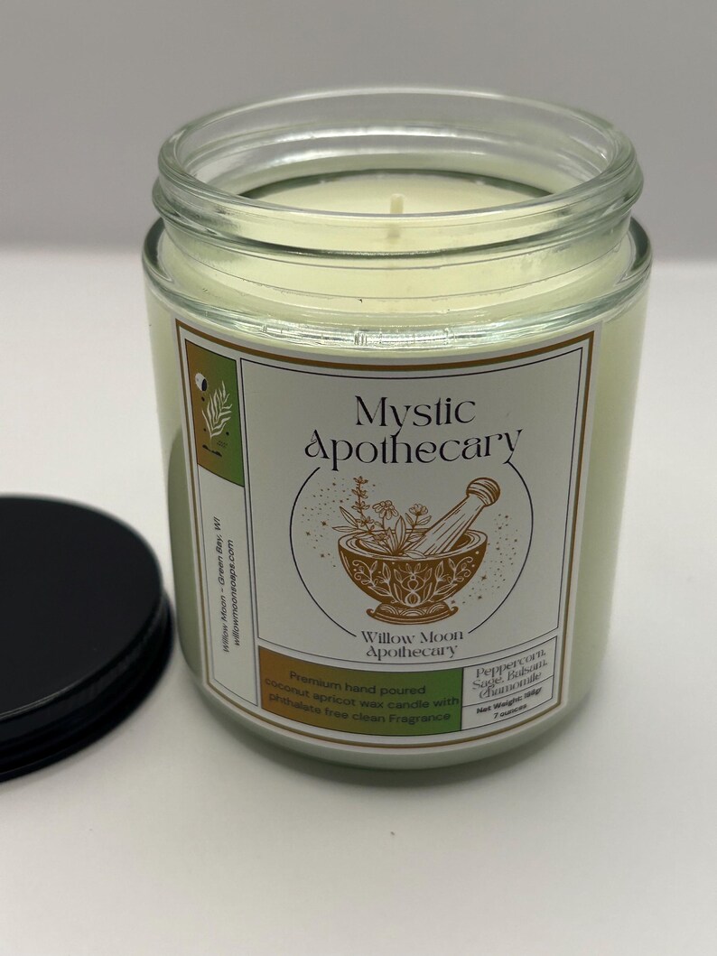 May include: A clear glass jar candle filled with off-white wax, featuring a label with the text Mystic Apothecary and an illustration of a mortar and pestle. The label lists Peppercorn, Sage, Balsam, Chamomile and a net weight of 7 ounces.