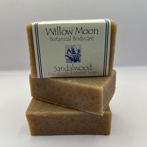 May include: Three bars of handcrafted sandalwood soap stacked on top of each other. The top bar has a label that reads "Willow Moon Botanical Bodycare" and "Sandalwood Handcrafted Herbal Soap".