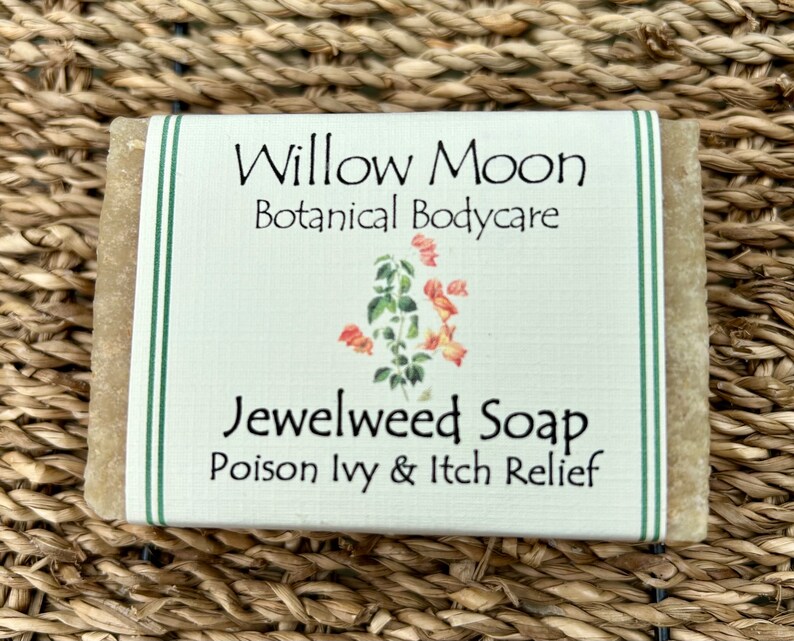 以下が含まれることがあります： 「Willow Moon Botanical Bodycare Jewelweed Soap Poison Ivy & Itch Relief」と書いてある白いラベルの石鹸。ラベルは緑色の縁取りと花のイラストが描かれている。