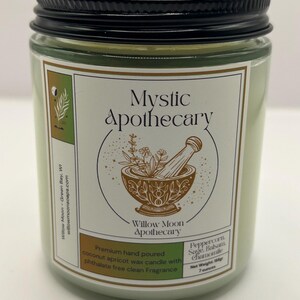 May include: A light green candle in a clear glass jar with a black metal lid. The label reads Mystic Apothecary, Willow Moon Apothecary, and lists Peppercorn, Sage, Balsam, Chamomile, with a net weight of 198g and 7 ounces, featuring a mortar and pestle.