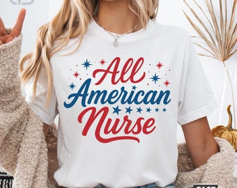 Puede incluir: Camiseta blanca con el texto "All American Nurse" en rojo y azul, con estrellas. El diseño tiene un tema patriótico. La camiseta tiene cuello redondo y parece estar hecha de un material suave.