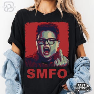 Könnte beinhalten: Schwarzes T-Shirt mit einer Grafik einer Person mit Brille, offenem Mund und erhobenem Mittelfinger. Die Grafik befindet sich auf rotem Hintergrund, darunter die roten Buchstaben "SMFO". Das T-Shirt hat eine lockere Passform.