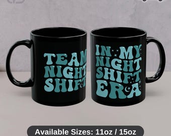 Può includere: Due tazze in ceramica nera con testo azzurro. La tazza a sinistra mostra le parole TEAM NIGHT SHIFT. La tazza a destra mostra le parole IN MY NIGHT SHIFT ERA con icone di stelle e lune. Il testo in basso riporta Available Sizes: 11oz / 15oz.