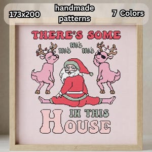 May include: A cross-stitch pattern in a light wooden frame featuring a central Santa Claus figure in a red suit sitting on the floor, flanked by two pink reindeer. The text reads THERE'S SOME HO'S HO'S HO'S IN THIS HOUSE. Dimensions are 173x200.