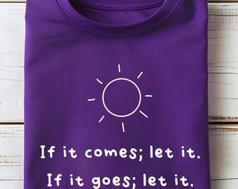 May include: A folded purple t-shirt with a white sun graphic and the text "If it comes; let it. If it goes; let it." The shirt is from Trendy Custom Sweaters, made in Texas.