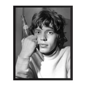 May include: Black and white framed portrait of a young man holding a bottle. The man has dark, wavy hair and is wearing a white turtleneck sweater. The bottle is clear and appears to contain a beverage.