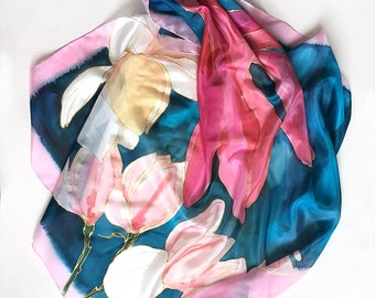Könnte beinhalten: Ein Seidentuch mit floralem Muster. Das Tuch ist blau, rosa und weiß mit einem Aquarell-Effekt. Die Blumen sind rosa und weiß mit goldenen Umrissen.