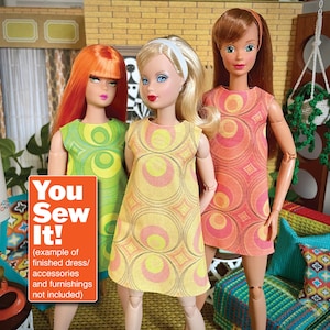 May include: Three dolls wearing different patterned dresses with geometric designs. The dolls are standing in front of a mid-century modern living room set. The text "You Sew It! (example of finished dress/accessories and furnishings not included)" is on a bright orange rectangle.