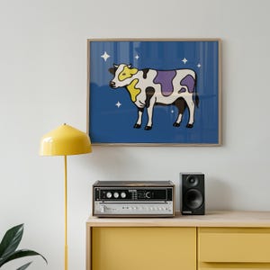 May include: A framed print of a cartoon cow with yellow and purple patches against a blue backdrop, with white stars. The artwork hangs above a yellow cabinet, a stereo, and a speaker.