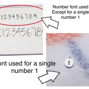 May include: A close-up of a silver charm with the number "1" engraved in a different font than the numbers "0123456789" written on a white surface.