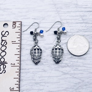 May include: Silver hockey mask earrings with blue and white beads. The earrings are about 1 inch long and are shown next to a ruler and a US quarter.
