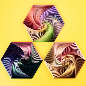 Könnte beinhalten: Drei sechseckige Wanddekorationen mit einem wirbelnden, mehrfarbigen Muster. Die Stücke sind aus einem strukturierten Material gefertigt und haben einen metallischen Glanz. Die Farben sind Rot, Lila, Grün, Blau und Gold.