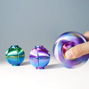 May include: Three spherical fidget toys with a metallic finish. One is green and blue, one is purple and blue, and the third is a spinning purple and blue sphere showing motion blur. Each toy features a segmented, multi-faceted surface design.
