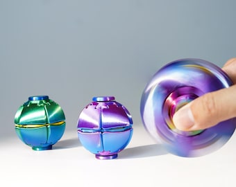 May include: Three spherical fidget toys with a metallic finish. One is green and blue, one is purple and blue, and the third is a spinning purple and blue sphere showing motion blur. Each toy features a segmented, multi-faceted surface design.