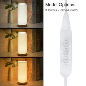 May include: A white table lamp with a cylindrical shade and a wooden base. The lamp has an inline control switch with buttons for power, brightness, and color temperature.