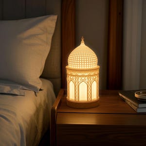May include: A white ceramic lamp with a geometric design in the shape of a dome. The lamp is on a wooden nightstand next to a bed.