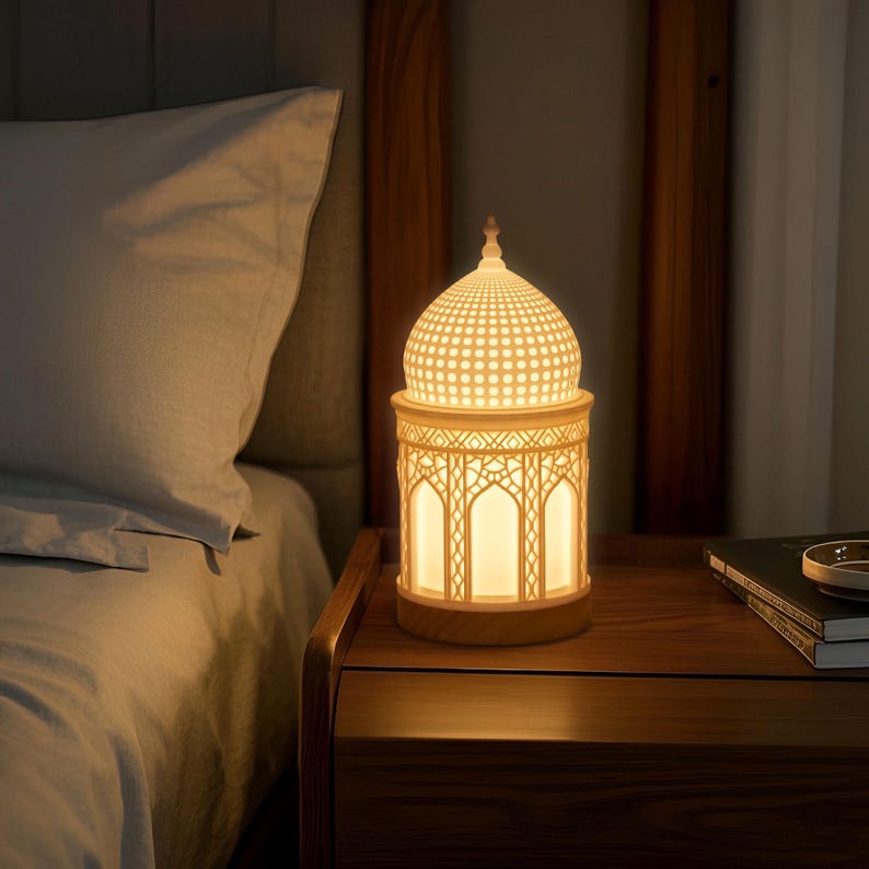 May include: A white ceramic lamp with a geometric design in the shape of a dome. The lamp is on a wooden nightstand next to a bed.