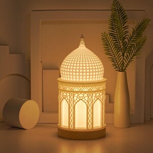 May include: White ceramic table lamp with a dome-shaped shade featuring a geometric pattern. The lamp base is a cylindrical shape with a decorative design and a wooden base.