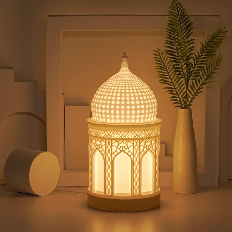 May include: White ceramic table lamp with a dome-shaped shade featuring a geometric pattern. The lamp base is a cylindrical shape with a decorative design and a wooden base.