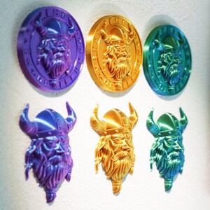Op de afbeelding: Een verzameling van zes Viking-thema wanddecoraties in verschillende kleuren. De ontwerpen omvatten drie ronde medaillons en drie Viking-hoofdsculpturen. Het kleurenpalet omvat paars, goud en teal, met metallic afwerkingen.