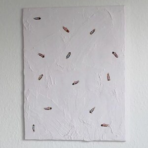 Könnte beinhalten: Abstraktes Kunstwerk auf einer weißen Leinwand. Die Leinwand hat eine strukturierte Oberfläche mit kleinen, farbigen, länglichen Formen, die darauf verstreut sind. Die Formen haben Farbtöne von Rosa, Blau und Braun.