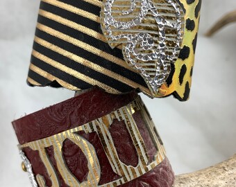 Choice of 2 leather cuffs bracelets.  One has Journey as focal point.  Other has leaf over two black and gold leather pieces.