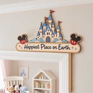 Puede incluir: Un adorno de madera para puerta que presenta un castillo beige con techos azules y banderas rojas, sobre un letrero horizontal con la inscripción "Happiest Place on Earth" en letra marrón oscuro, flanqueado por dos siluetas de orejas de Mickey Mouse.