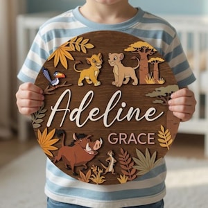 May include: A round wooden sign with a Lion King theme, featuring the names "Adeline Grace" in cursive. The sign includes cartoon images of Simba, Nala, Timon, Pumbaa, and other jungle elements. The sign is brown with colorful accents.
