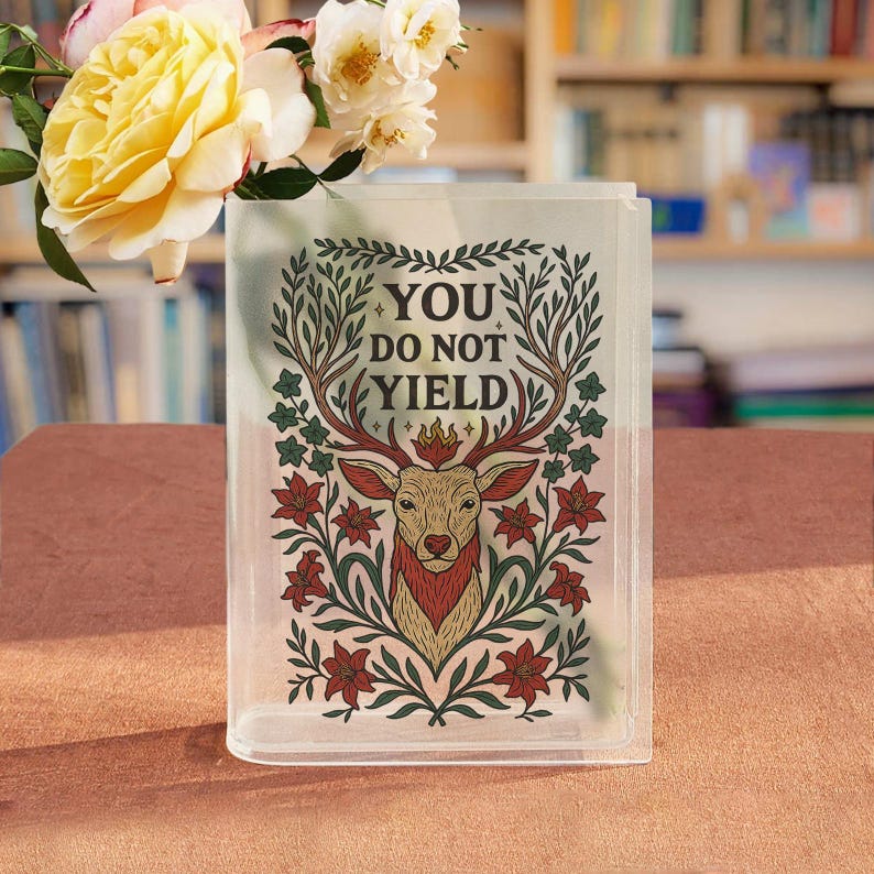May include: A clear rectangular vase with the words "YOU DO NOT YIELD" and a deer illustration. The deer is brown and red, surrounded by green leaves and red flowers. Yellow roses and white flowers are in the vase.