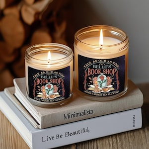Può includere: Due barattoli di vetro per candele con un'etichetta in bianco e nero che dice "Tale as old as time Belle's Book Shop" con un design floreale. L'etichetta dice anche "Libri, Candele, Tè, Fiori".