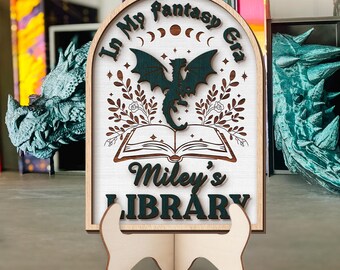 May include: A wooden bookend with a white background and a green dragon design. The bookend has the text "In My Fantasy Era" at the top and "Miley's Library" at the bottom.