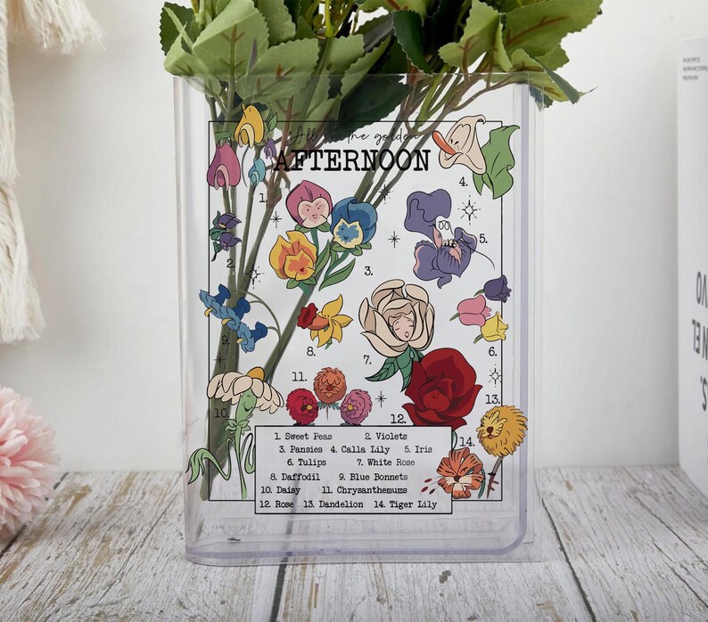 May include: Clear rectangular vase with a floral design and the text "Afternoon." The vase features illustrations of various flowers, including sweet peas, pansies, and roses. Green foliage is inside the vase.