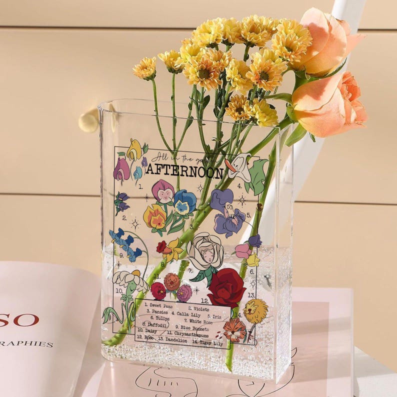 May include: A clear rectangular vase with a floral design and the text "All in the Afternoon" holds yellow chrysanthemums and peach roses. The vase has a decorative floral illustration with flower names.