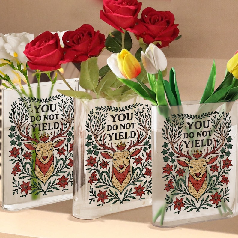 May include: Three clear glass vases with a deer and floral design, and the text "YOU DO NOT YIELD". The vases hold red roses, yellow and white tulips, and other greenery. The vases are rectangular and have a slight curve.