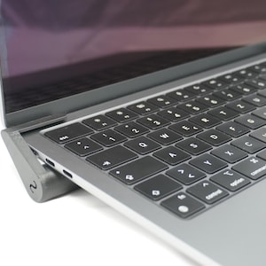Op de afbeelding: Een zilveren laptop met een zwart toetsenbord en een trackpad. De laptop staat op een grijze standaard.