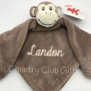 May include: A brown plush monkey-faced security blanket with the name "Landon" embroidered in white. The blanket has a soft, textured feel and the text "Country Club Gifts" is also embroidered on the blanket.