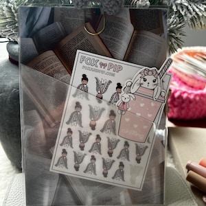 Könnte beinhalten: Eine transparente Planertasche mit einem goldenen Clip und einer grauen Schleife. Im Inneren befinden sich Buchseiten und ein Stickerbogen mit Illustrationen eines Hasen und eines Mädchens. Der Stickerbogen trägt den Text "FOX & PIP".