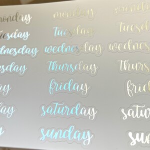 May include: A sheet of clear stickers with the days of the week written in a cursive font. The stickers are iridescent and have a holographic finish. The days of the week are: Monday, Tuesday, Wednesday, Thursday, Friday, Saturday, and Sunday.