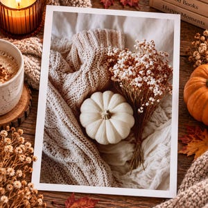 May include: A white pumpkin rests on a beige cable-knit sweater next to a bouquet of dried white baby's breath flowers. The scene is captured in a rectangular print with a white border, evoking a seasonal autumn aesthetic with soft textures.