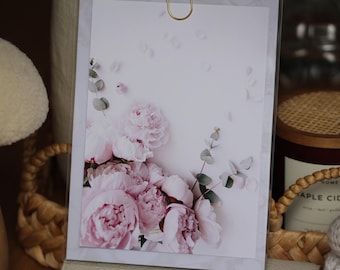Puede incluir: Una impresión enmarcada con un ramo de peonías rosas y hojas de eucalipto sobre un fondo blanco. Las flores están dispuestas en un estilo suelto y natural, y las hojas añaden un toque de verdor. La impresión es perfecta para añadir un toque de elegancia a cualquier habitación.