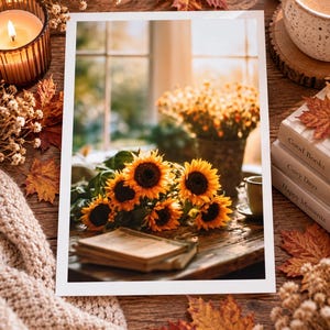 May include: A rectangular print featuring a bouquet of bright yellow sunflowers resting on a wooden table next to a closed book. The scene includes a window in the background, a lit candle, a coffee mug, and a stack of books labelled Good Books, Cozy Days, and Happy Moments.
