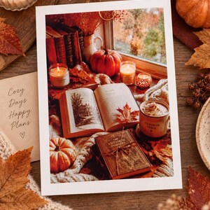 Könnte beinhalten: Ein rechteckiger Druck mit einer herbstlichen Szene, einem aufgeschlagenen Buch, einem geschlossenen Buch mit dem Titel Autumn Whispers, Kürbissen, Kerzen und einer Tasse mit der Aufschrift Pumpkin Spice. Links steht eine Karte mit dem Text Cozy Days Happy Plans und einem Herz.