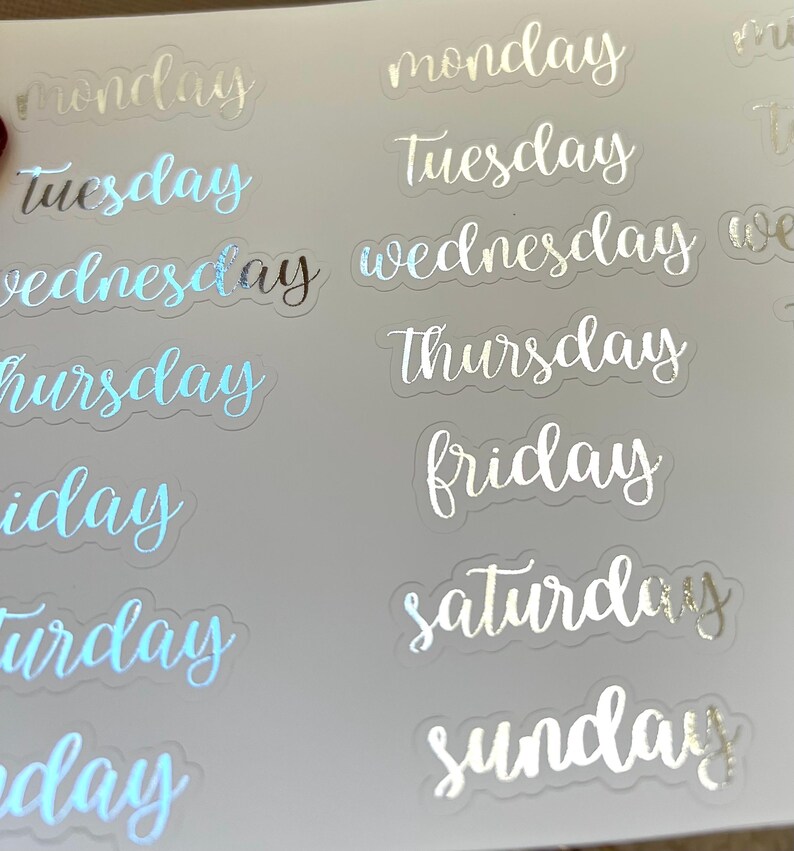May include: A sheet of clear stickers with silver foil lettering for each day of the week. The stickers are designed for use in planners and journals.