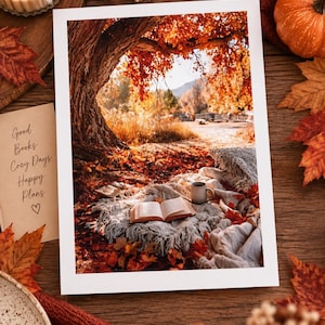 May include: A rectangular print featuring an autumn scene with a large tree, fallen leaves, and a cozy outdoor reading nook with an open book and a mug on a textured blanket. A separate card displays the text: Good Books, Cozy Days, Happy Plans.